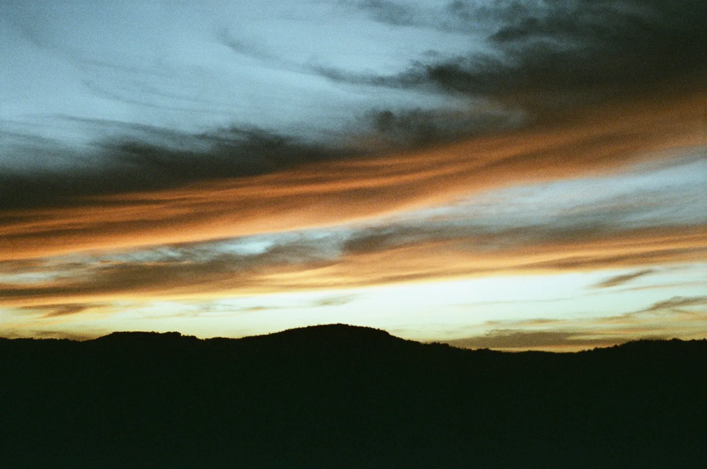 Orange sunset clouds over dark hills